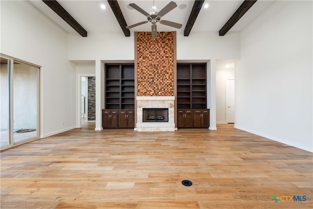 unfurnished living room featuring ceiling fan, a stone fireplace, beam ceiling, and light hardwood / wood-style flooring