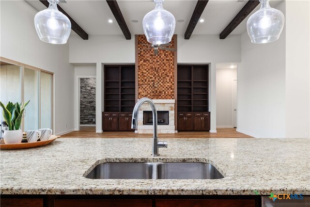 kitchen with beamed ceiling, sink, light hardwood / wood-style flooring, and light stone counters