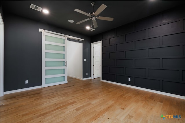 unfurnished bedroom featuring light wood-type flooring, a barn door, and ceiling fan