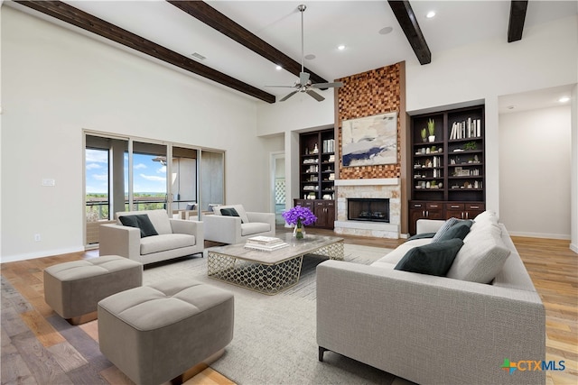 living room featuring ceiling fan, beam ceiling, a large fireplace, hardwood / wood-style floors, and a towering ceiling