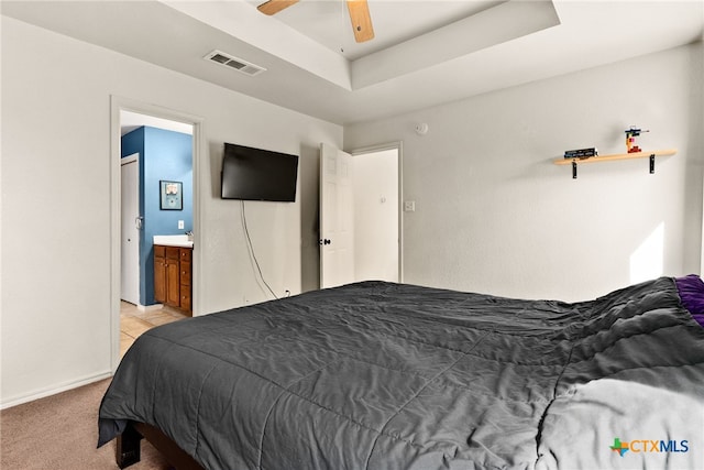 bedroom with light carpet, ceiling fan, a tray ceiling, and connected bathroom