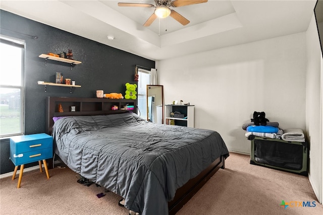 bedroom with light colored carpet, ceiling fan, and a raised ceiling