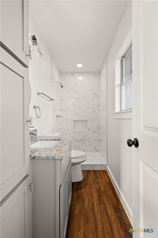 bathroom featuring toilet, wood-type flooring, vanity, and a tile shower