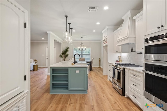 kitchen with white cabinets, appliances with stainless steel finishes, light hardwood / wood-style floors, and an island with sink