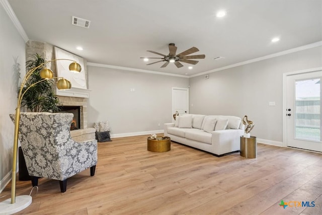 living room with a fireplace, light hardwood / wood-style floors, ceiling fan, and crown molding