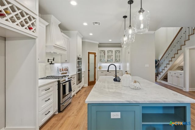 kitchen featuring sink, custom range hood, white cabinetry, appliances with stainless steel finishes, and a large island with sink