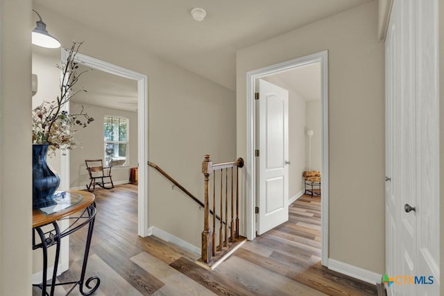 corridor featuring an upstairs landing, wood finished floors, and baseboards
