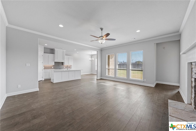 unfurnished living room featuring a fireplace, ceiling fan with notable chandelier, crown molding, and dark hardwood / wood-style flooring