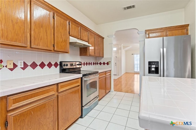 kitchen with backsplash, tile countertops, light tile patterned floors, and stainless steel appliances