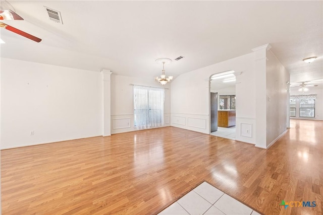 empty room featuring ceiling fan with notable chandelier, light hardwood / wood-style floors, and ornate columns