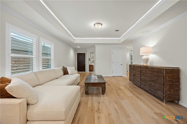 living room with ornamental molding, a tray ceiling, and light wood-type flooring