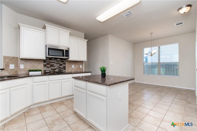 kitchen with white cabinetry, backsplash, dark stone countertops, a center island, and light tile patterned flooring