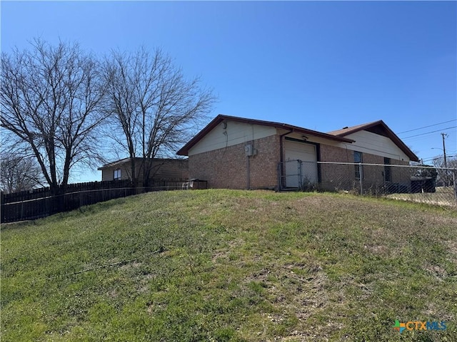 view of side of property featuring a garage, fence, brick siding, and a yard