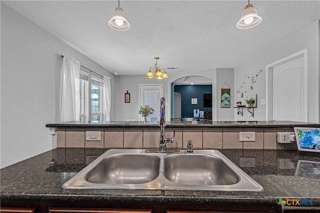 kitchen with a sink, dark stone counters, a textured ceiling, and hanging light fixtures