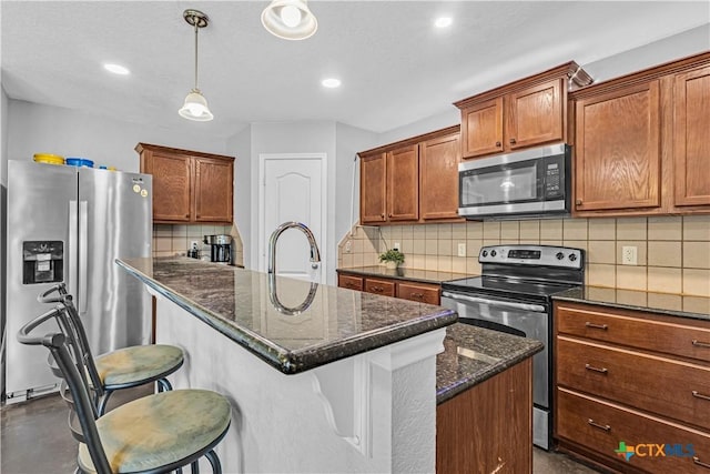 kitchen featuring a kitchen bar, a kitchen island with sink, tasteful backsplash, stainless steel appliances, and brown cabinetry