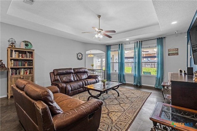 living room with baseboards, visible vents, a tray ceiling, arched walkways, and ceiling fan