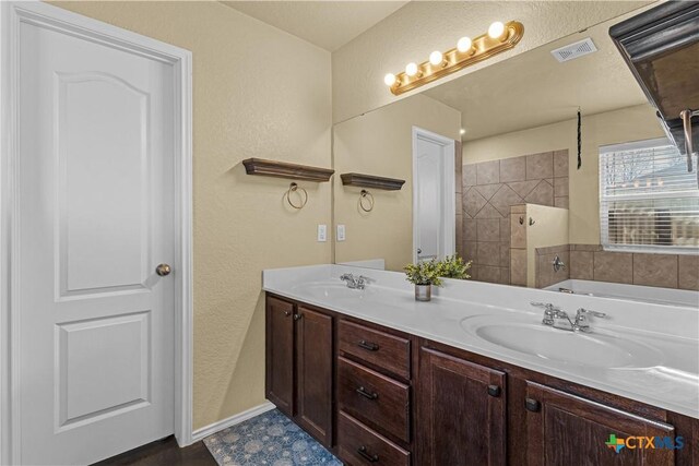 full bathroom with double vanity, a tub to relax in, visible vents, and a sink