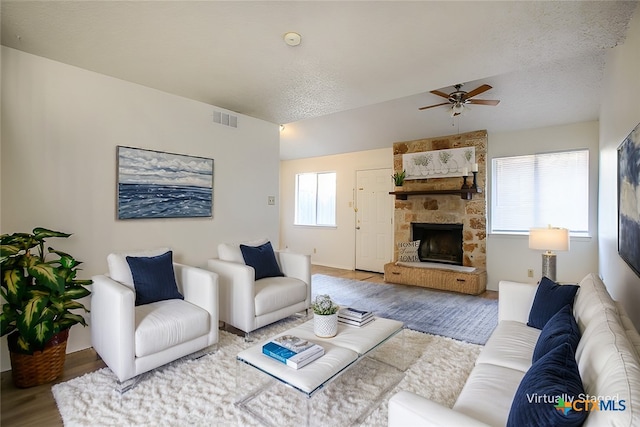 living room with a textured ceiling, ceiling fan, hardwood / wood-style flooring, and a stone fireplace