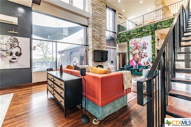 living room with a towering ceiling, dark hardwood / wood-style floors, a stone fireplace, and a wall mounted AC