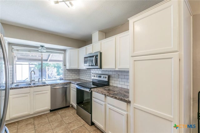 kitchen with dark countertops, decorative backsplash, appliances with stainless steel finishes, white cabinetry, and a sink