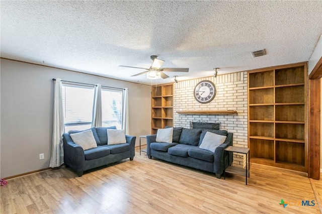 living room with a fireplace, visible vents, ceiling fan, a textured ceiling, and light wood-type flooring