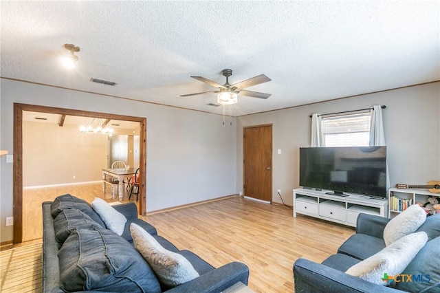 living room featuring visible vents, a textured ceiling, wood finished floors, baseboards, and ceiling fan with notable chandelier