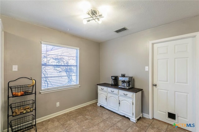 interior space with light tile patterned floors, a textured ceiling, visible vents, and baseboards