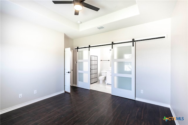 unfurnished room featuring a raised ceiling, dark wood-type flooring, a barn door, and ceiling fan