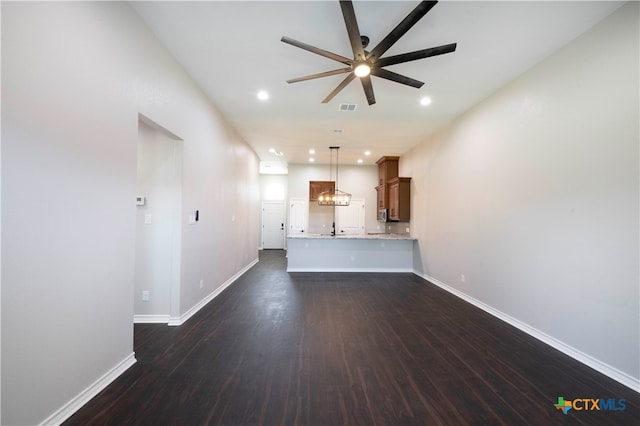 unfurnished living room featuring ceiling fan with notable chandelier and dark hardwood / wood-style flooring