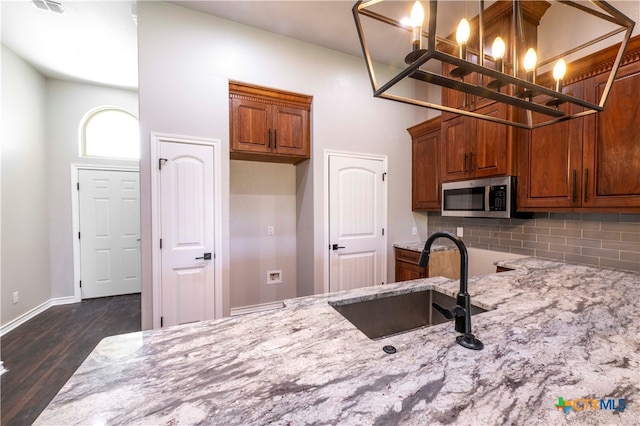 kitchen with light stone counters, dark hardwood / wood-style floors, pendant lighting, decorative backsplash, and sink