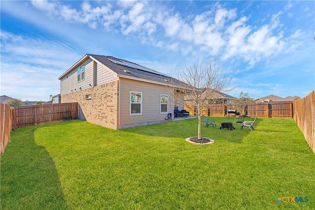 back of house with a yard, a fire pit, and solar panels