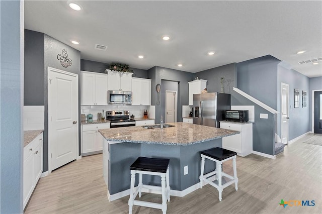 kitchen with white cabinetry, stainless steel appliances, sink, and a center island with sink