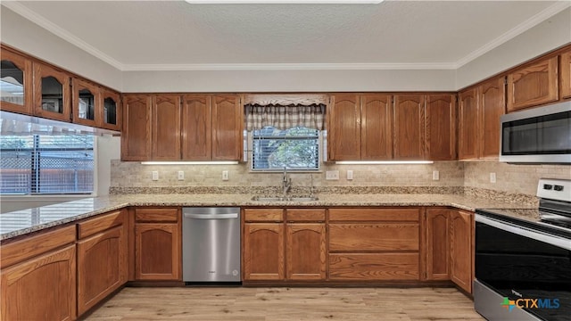 kitchen featuring light stone countertops, appliances with stainless steel finishes, crown molding, sink, and light hardwood / wood-style floors