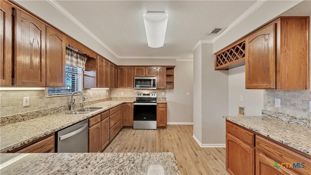 kitchen featuring light stone countertops, appliances with stainless steel finishes, tasteful backsplash, sink, and light hardwood / wood-style flooring