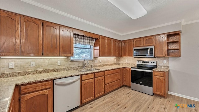 kitchen featuring sink, light hardwood / wood-style flooring, ornamental molding, light stone countertops, and stainless steel appliances