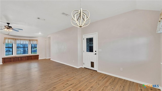 empty room with vaulted ceiling, wood-type flooring, and ceiling fan with notable chandelier