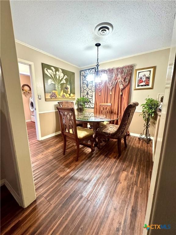 dining area featuring dark hardwood / wood-style floors, an inviting chandelier, washer / clothes dryer, and crown molding