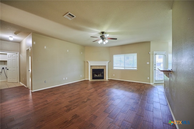 unfurnished living room with a tiled fireplace, wood-type flooring, ceiling fan, and a textured ceiling