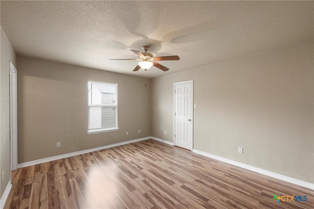 empty room with baseboards, a ceiling fan, a textured ceiling, and wood finished floors