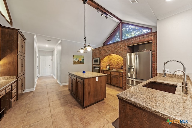 kitchen with stainless steel appliances, brick wall, sink, light stone countertops, and a center island