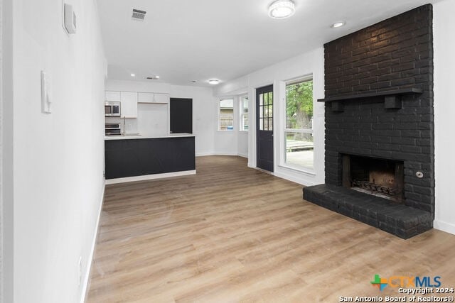 unfurnished living room featuring a brick fireplace and light hardwood / wood-style flooring