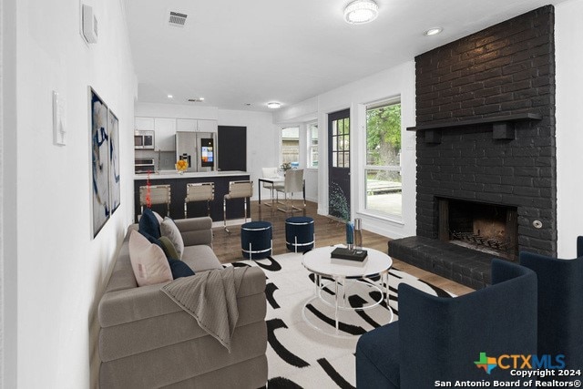 living room featuring wood-type flooring and a brick fireplace