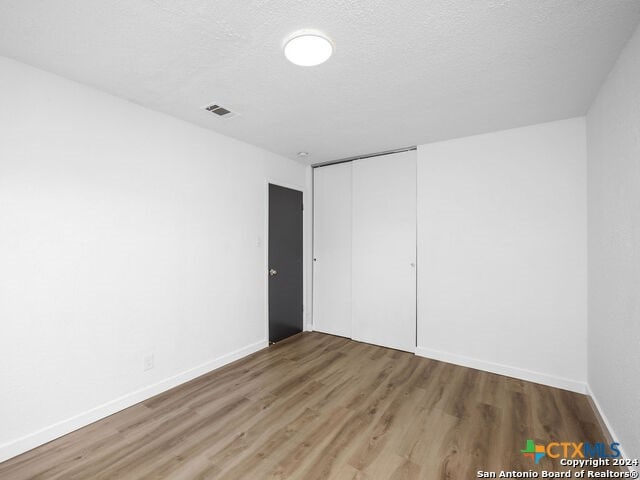 unfurnished bedroom featuring a closet, wood-type flooring, and a textured ceiling