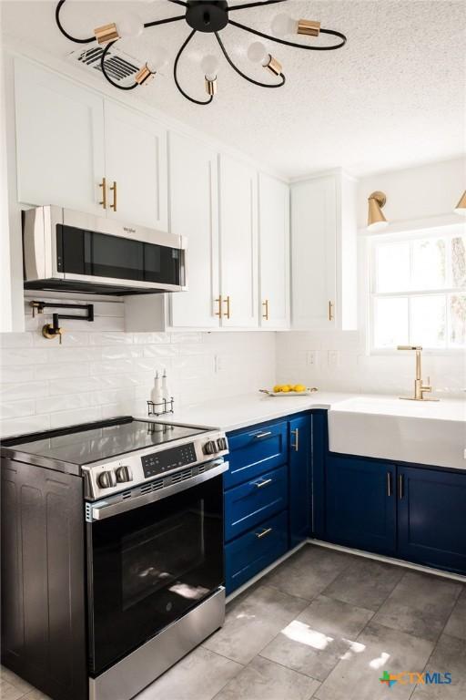 1004 Buena Vista Ave, Victoria, TX 77901 - kitchen featuring stainless steel appliances, blue cabinets, a sink, backsplash, and white cabinetry