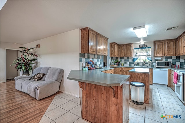 kitchen featuring a center island, light tile patterned floors, tasteful backsplash, a breakfast bar area, and white appliances