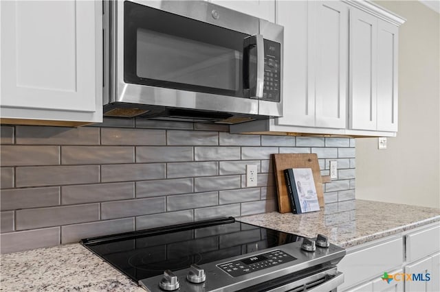 kitchen with white cabinets, tasteful backsplash, light stone counters, and stainless steel appliances