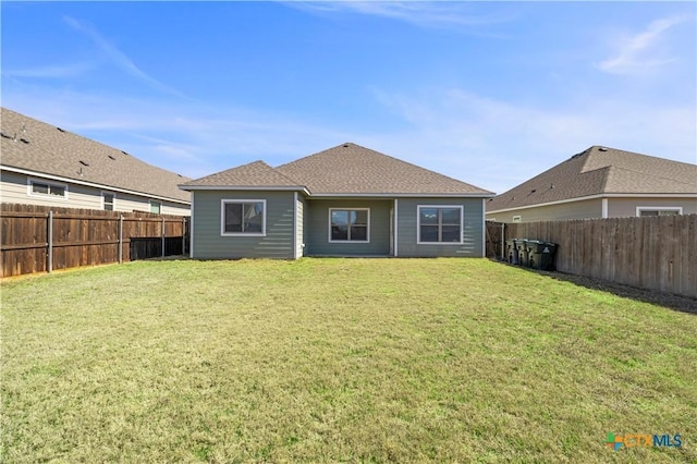 rear view of property with a fenced backyard, a shingled roof, and a yard