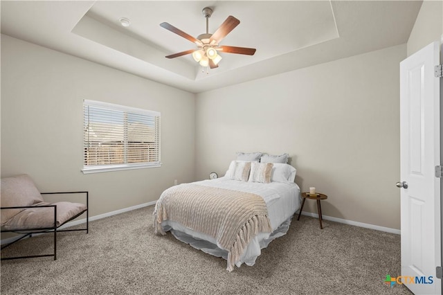 carpeted bedroom with a raised ceiling, a ceiling fan, and baseboards