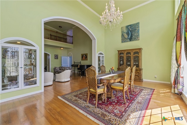 dining room with a high ceiling, wood-type flooring, a notable chandelier, and crown molding