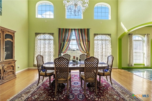 dining space with a towering ceiling, wood-type flooring, and an inviting chandelier